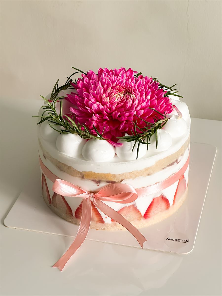 Strawberry cream cake topped with a fresh chrysanthemum and rosemary, finished with a pink ribbon